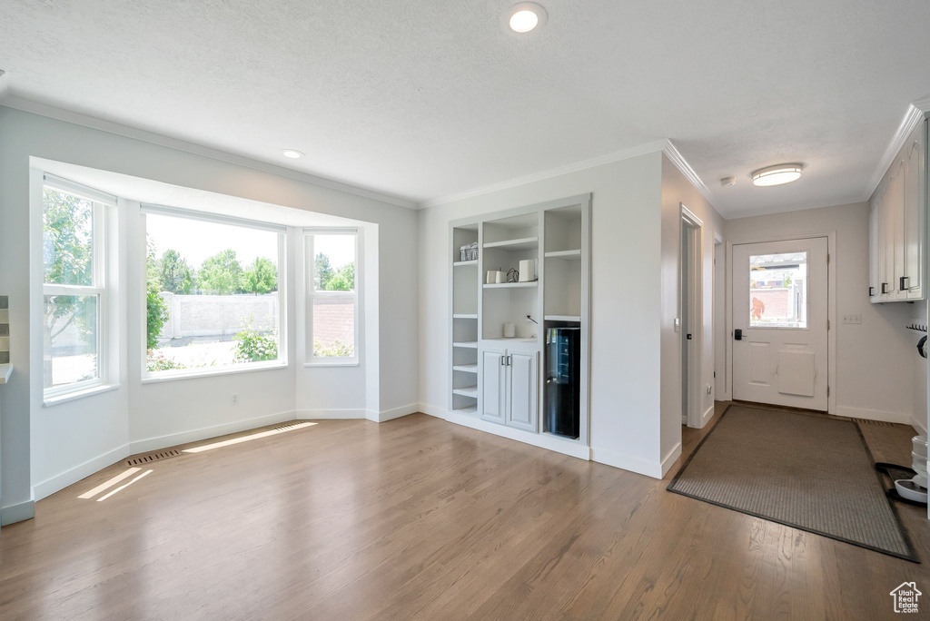 Unfurnished living room with crown molding, wood finished floors, built in shelves, and recessed lighting