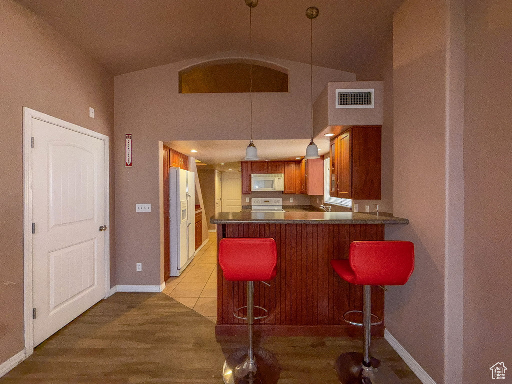 Kitchen with white appliances, a peninsula, high vaulted ceiling, brown cabinetry, and pendant lighting