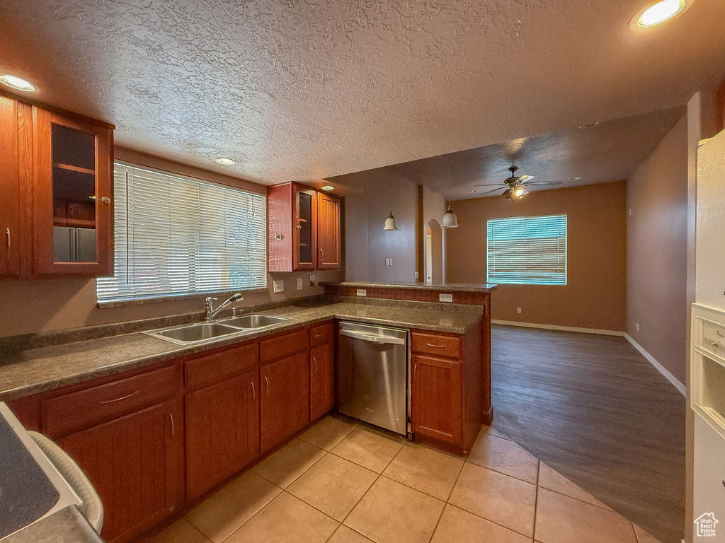 Kitchen featuring stainless steel dishwasher, a peninsula, brown cabinetry, a ceiling fan, and light tile patterned floors