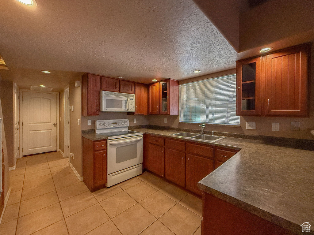 Kitchen with white appliances, dark countertops, light tile patterned flooring, recessed lighting, and brown cabinetry