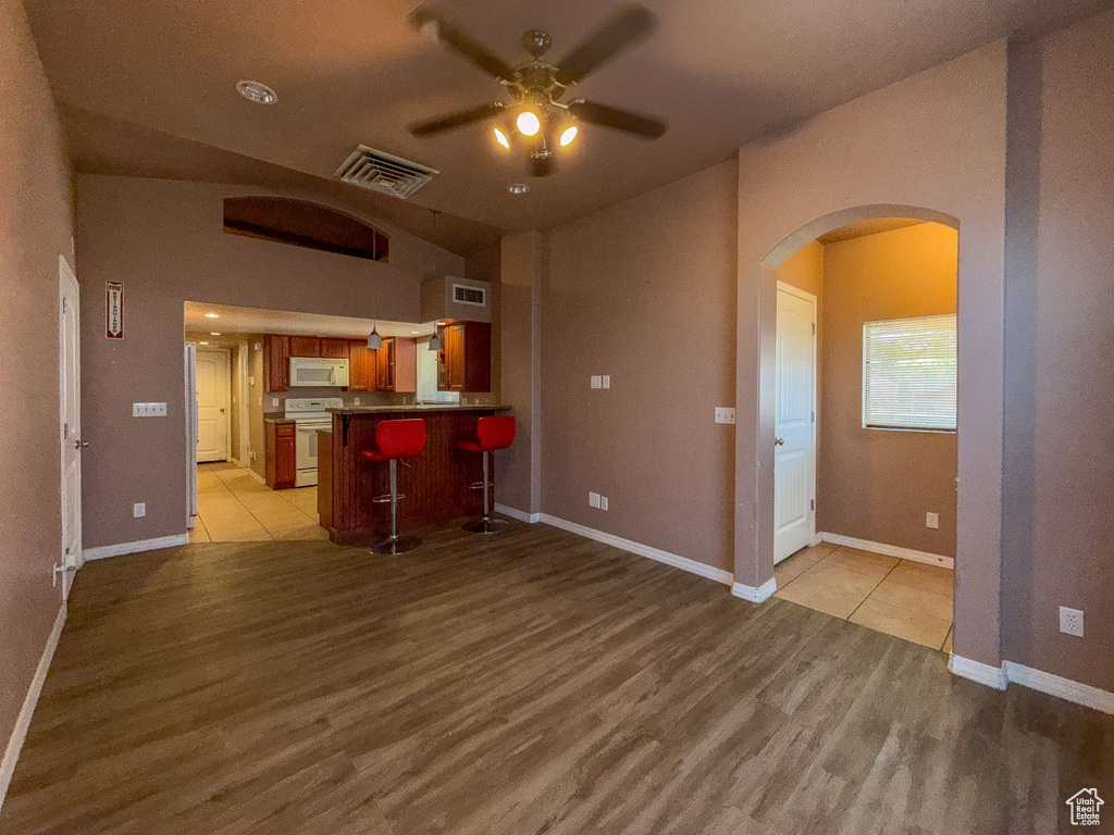 Kitchen featuring white appliances, arched walkways, light wood finished floors, a ceiling fan, and a peninsula