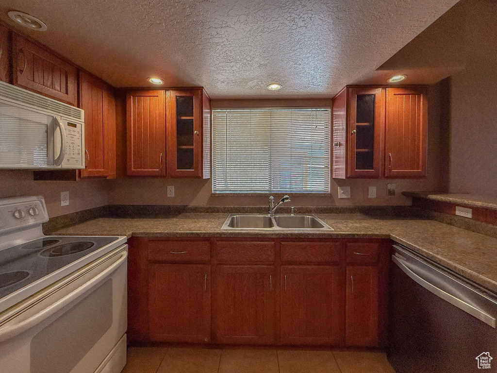 Kitchen featuring white appliances, a textured ceiling, brown cabinets, glass insert cabinets, and light tile patterned floors