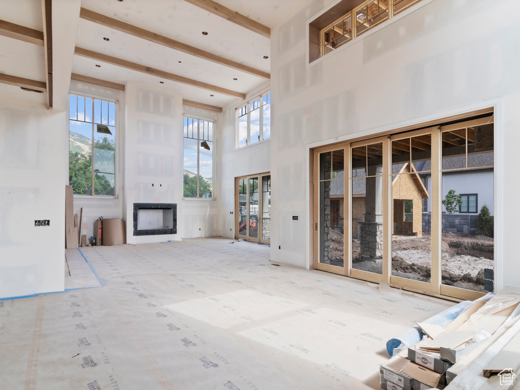 Unfurnished living room with a towering ceiling, a fireplace, and beamed ceiling