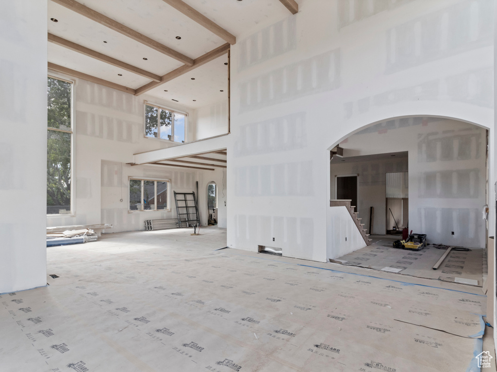 Unfurnished living room with a towering ceiling, arched walkways, stairway, and beamed ceiling
