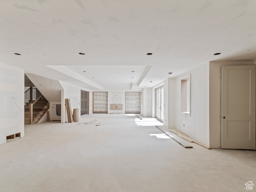 Unfurnished living room featuring a raised ceiling and stairway