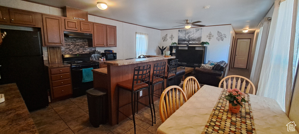 Kitchen featuring black appliances, ceiling fan, under cabinet range hood, brown cabinets, and dark tile patterned flooring