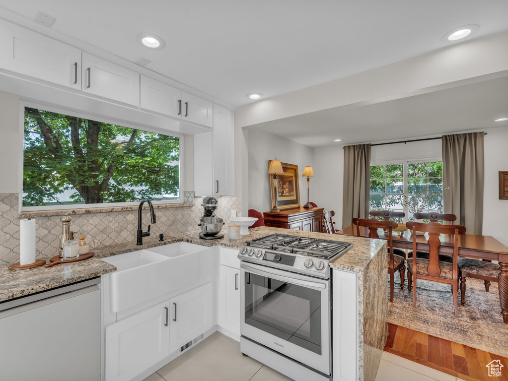Kitchen featuring gas range, dishwasher, a peninsula, white cabinetry, and light stone countertops