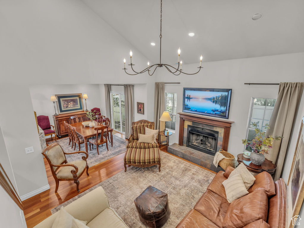 Living area with wood finished floors, a tile fireplace, a chandelier, high vaulted ceiling, and recessed lighting
