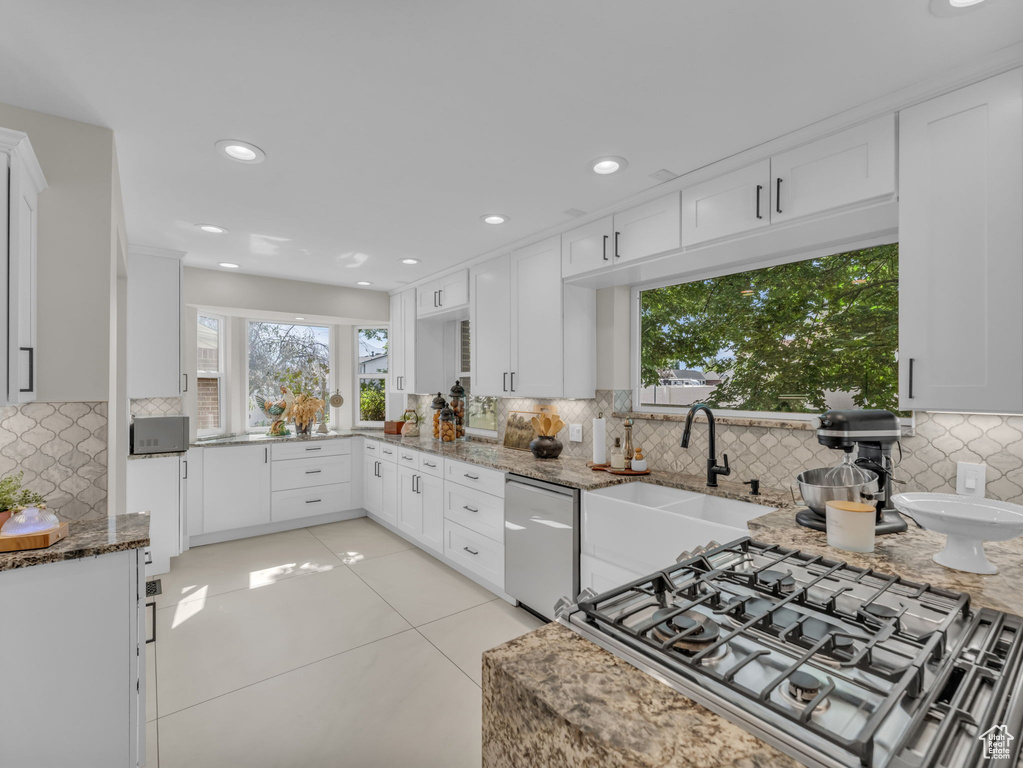 Kitchen with tasteful backsplash, dishwasher, cooktop, light stone countertops, and white cabinetry