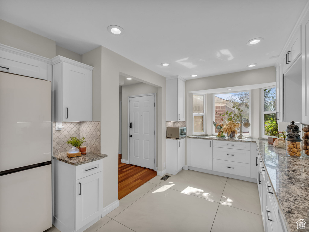 Kitchen with freestanding refrigerator, white cabinetry, tasteful backsplash, light stone counters, and recessed lighting
