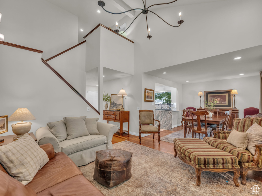 Living room with light wood-style flooring, a towering ceiling, stairs, a chandelier, and recessed lighting