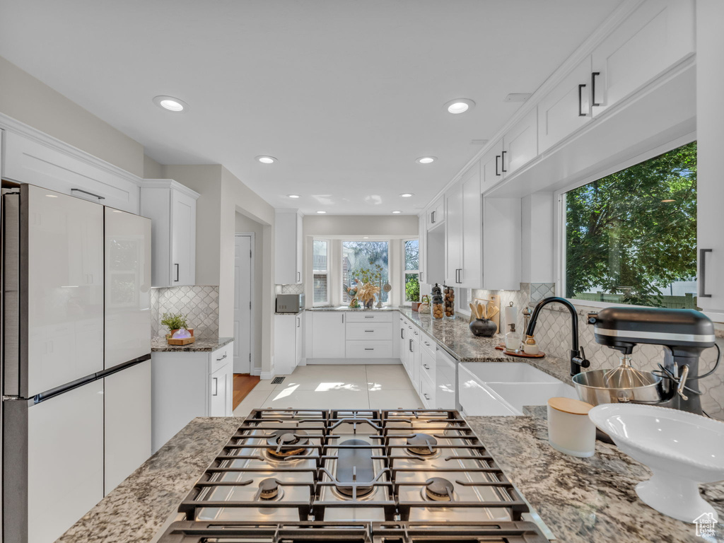 Kitchen with freestanding refrigerator, stainless steel gas stovetop, tasteful backsplash, white cabinets, and light stone countertops
