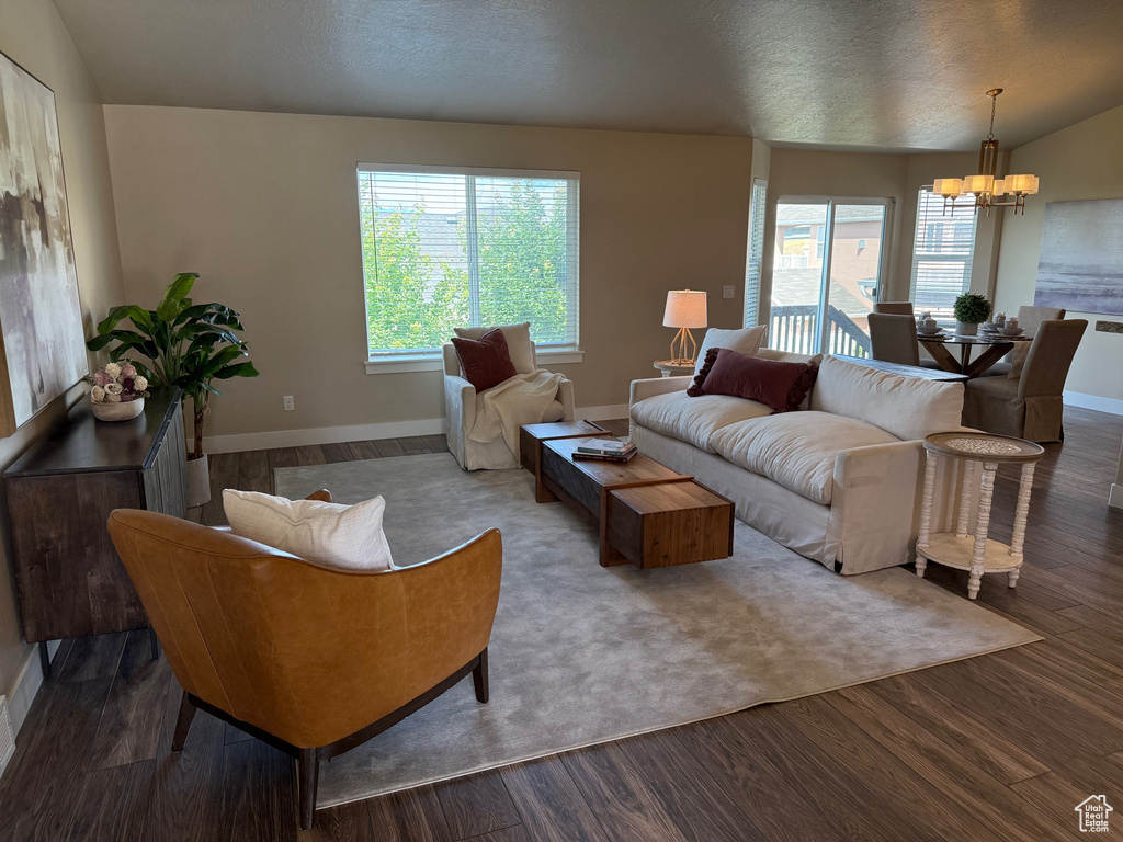 Living area featuring a chandelier, plenty of natural light, wood finished floors, a textured ceiling, and vaulted ceiling