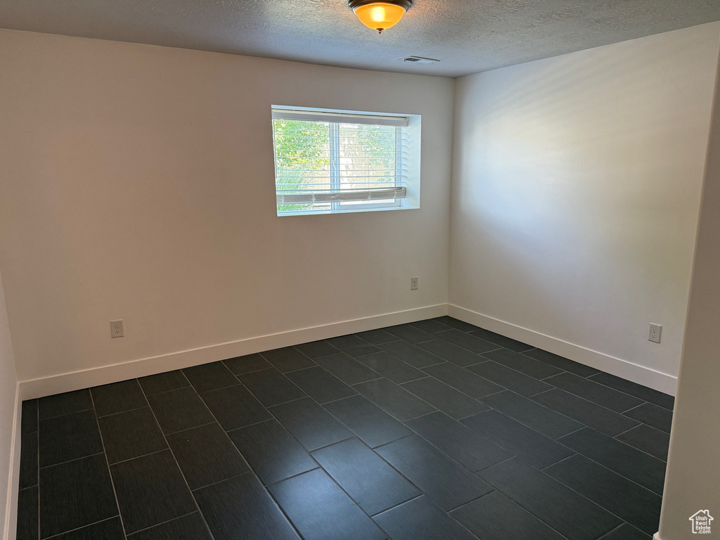 Empty room featuring a textured ceiling and dark tile patterned flooring