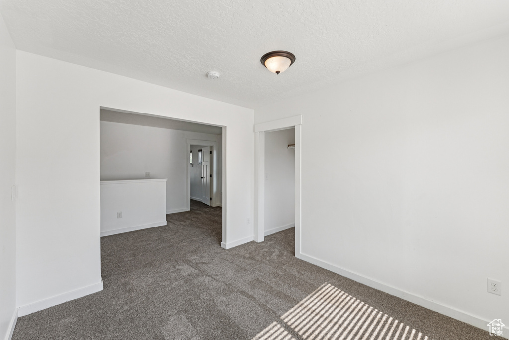 Carpeted empty room featuring a textured ceiling and a smoke detector