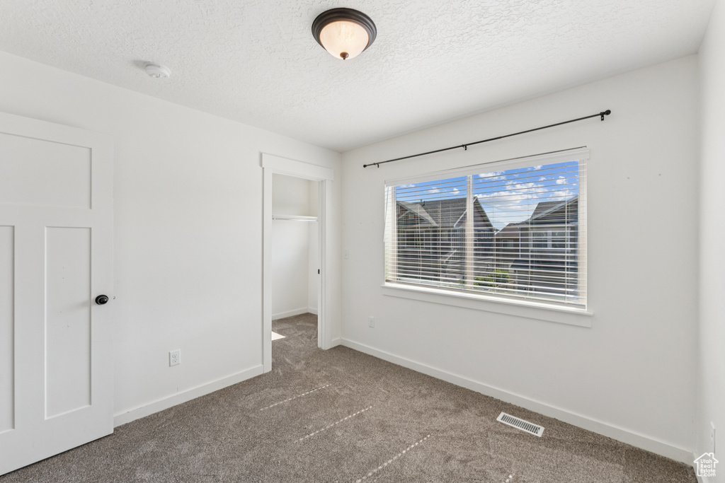 Unfurnished bedroom featuring carpet flooring, a textured ceiling, a spacious closet, and a closet