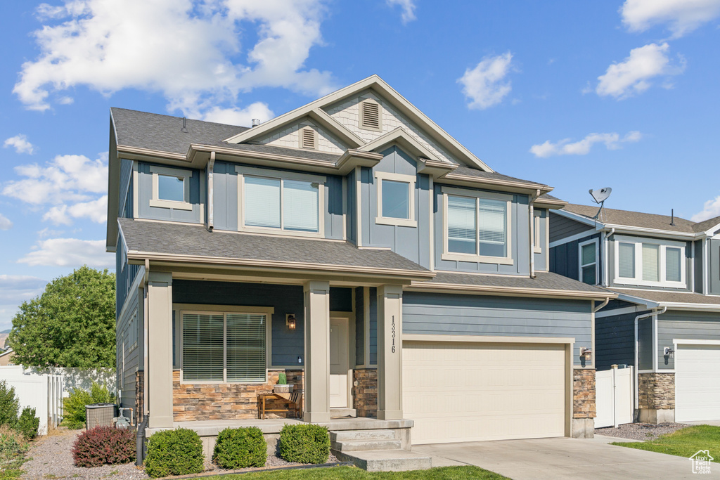 View of front facade with stone siding, a garage, board and batten siding, covered porch, and concrete driveway