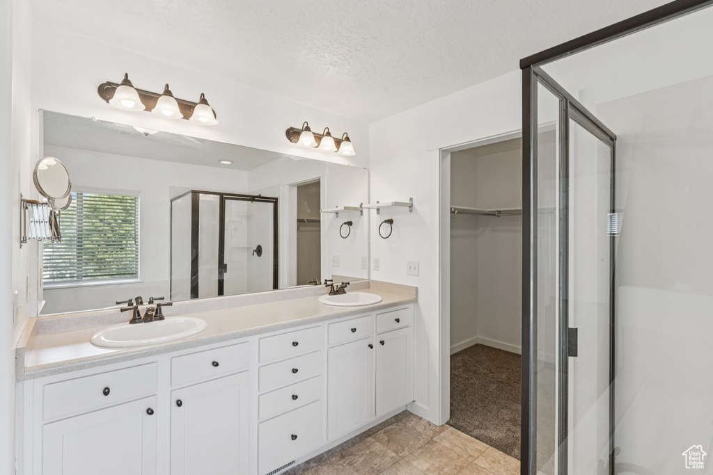 Full bathroom featuring a stall shower, a spacious closet, double vanity, and a textured ceiling