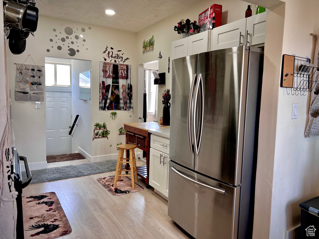 Kitchen featuring freestanding refrigerator, white cabinetry, light wood-type flooring, light countertops, and a textured ceiling