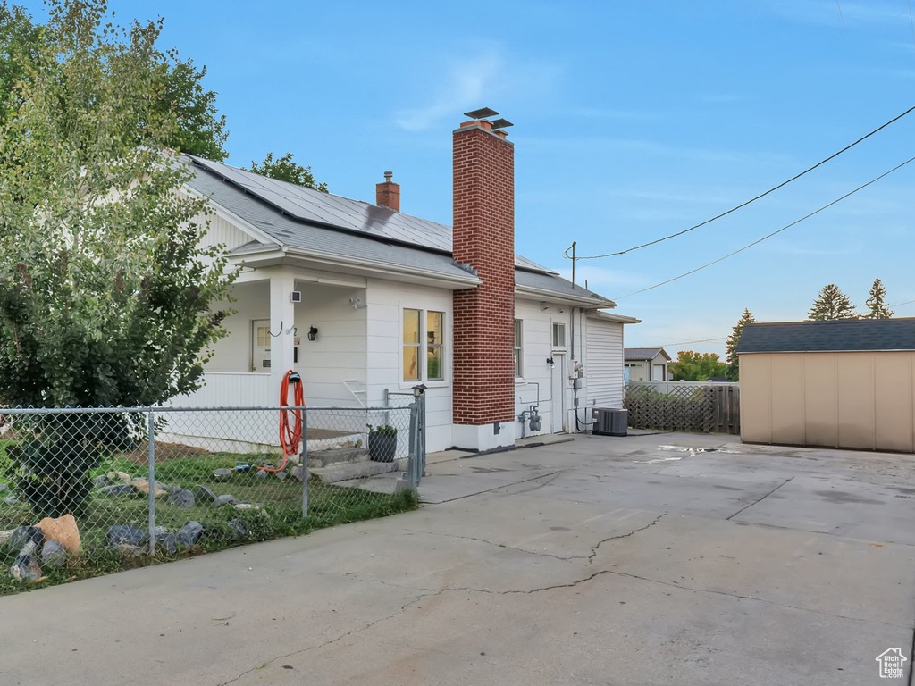 View of front of home with solar panels, a chimney, and a shed