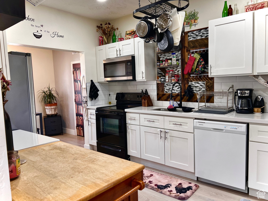 Kitchen featuring appliances with stainless steel finishes, light countertops, decorative backsplash, white cabinets, and light wood-type flooring