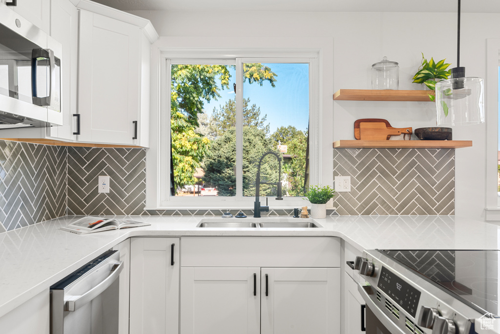 Kitchen with appliances with stainless steel finishes, backsplash, light countertops, and open shelves