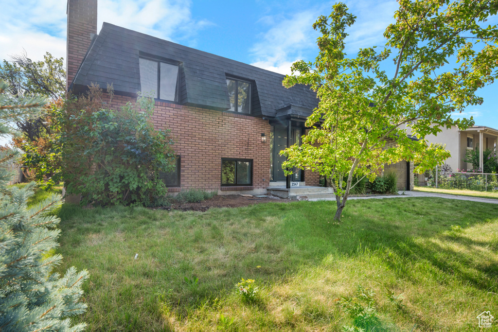 View of front of house featuring brick siding, a chimney, and a front lawn