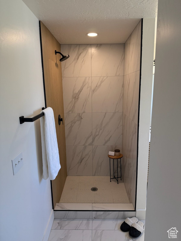Bathroom featuring marble look tiles, a tile shower, a textured ceiling, and recessed lighting