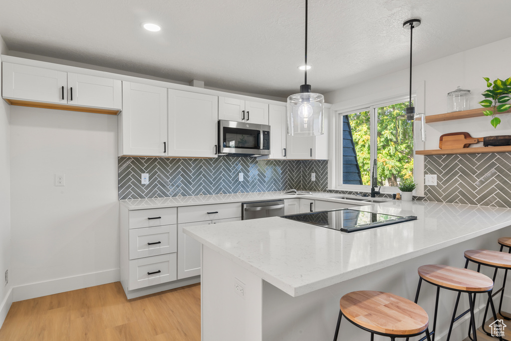 Kitchen featuring appliances with stainless steel finishes, a peninsula, white cabinetry, light wood-style flooring, and a kitchen bar
