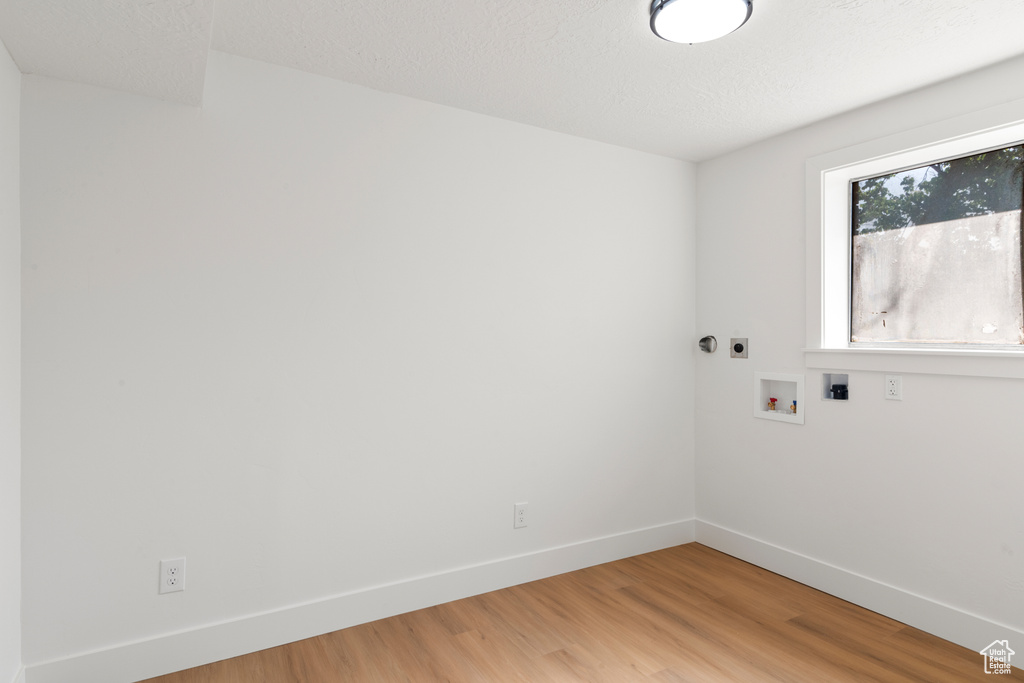 Washroom with electric dryer hookup, hookup for a washing machine, and light wood-style flooring