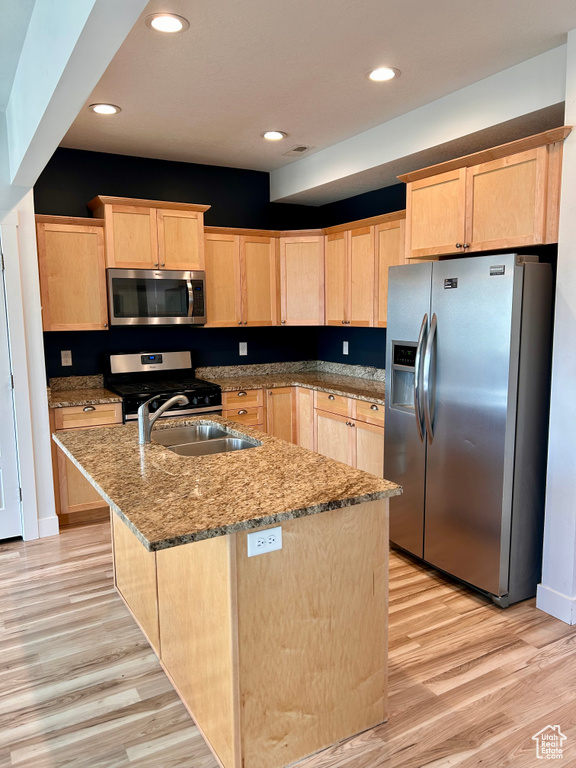 Kitchen with stainless steel appliances, light brown cabinetry, light wood-type flooring, an island with sink, and recessed lighting