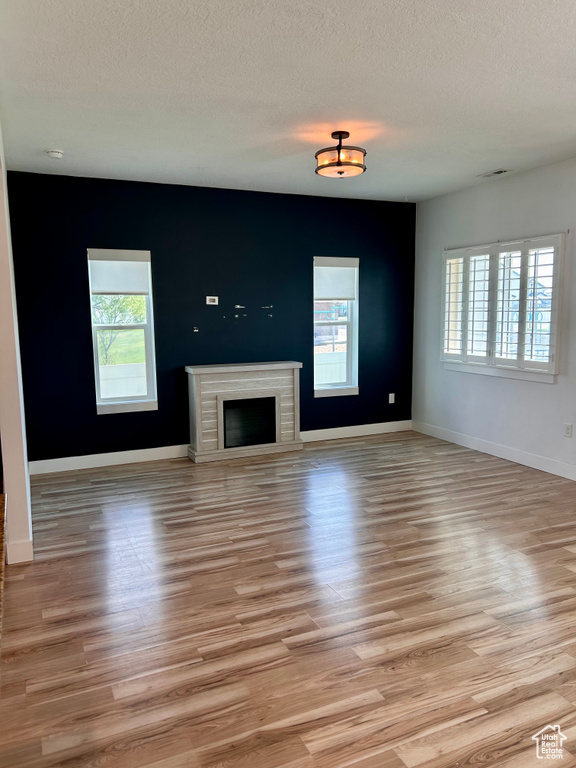 Unfurnished living room with light wood-style flooring, a textured ceiling, and a fireplace