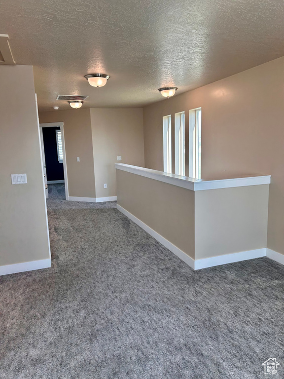 Carpeted spare room featuring a textured ceiling and baseboards
