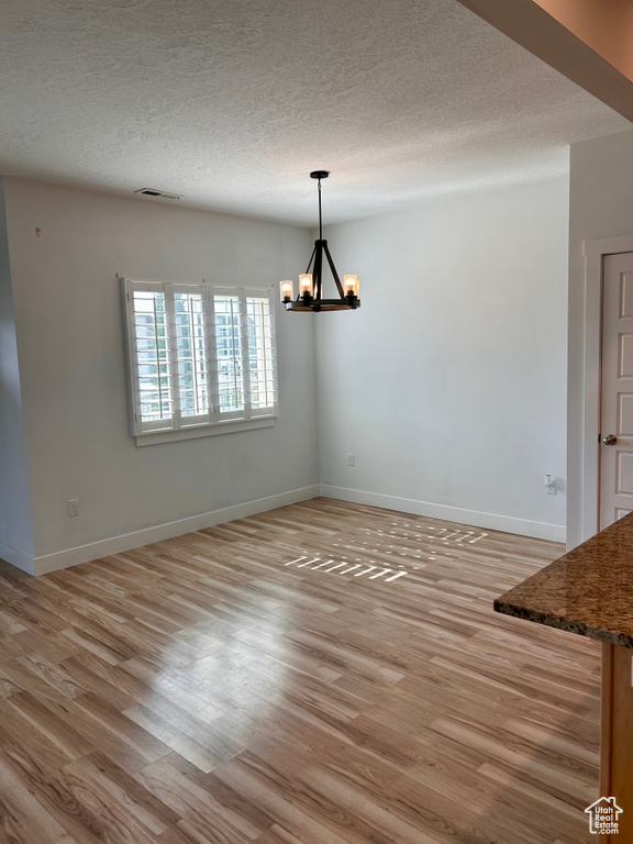 Unfurnished dining area with a chandelier, light wood-type flooring, and a textured ceiling