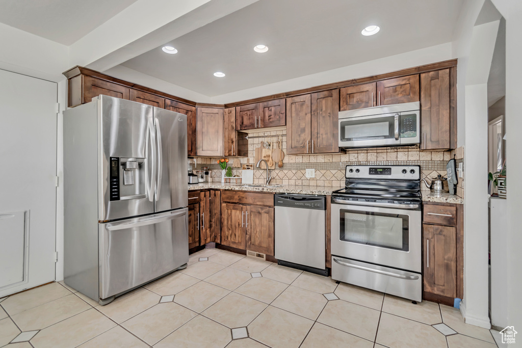 Kitchen featuring appliances with stainless steel finishes, backsplash, light stone counters, and recessed lighting