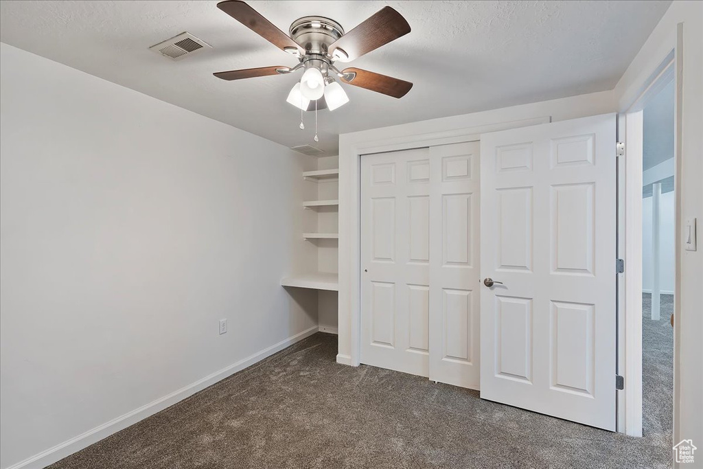 Unfurnished bedroom featuring dark colored carpet, a closet, a ceiling fan, and a textured ceiling