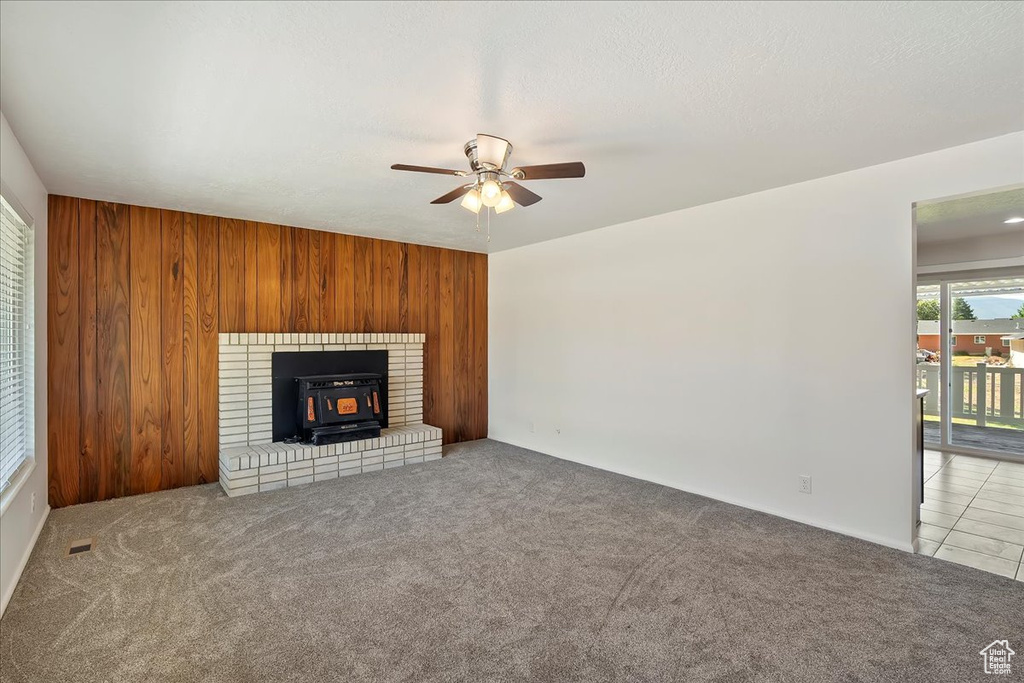 Unfurnished living room featuring a wood stove, ceiling fan, carpet flooring, and wooden walls