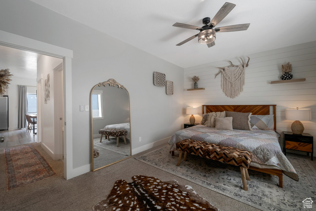 Carpeted bedroom with freestanding refrigerator, arched walkways, a ceiling fan, and wooden walls