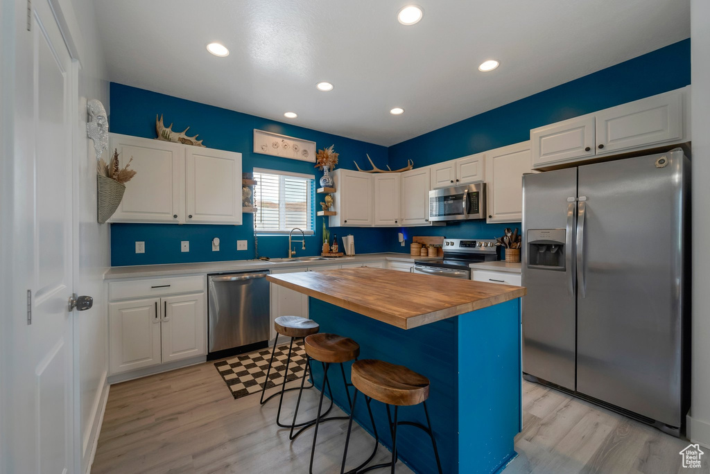 Kitchen with appliances with stainless steel finishes, wood counters, white cabinets, a breakfast bar, and recessed lighting