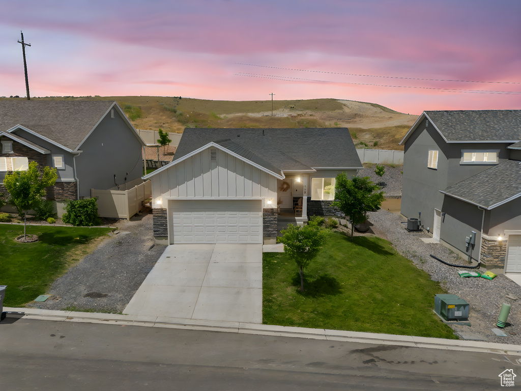 Single story home with board and batten siding, an attached garage, driveway, a mountain view, and stone siding