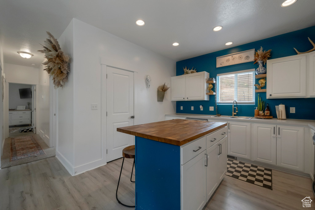 Kitchen with wood counters, light wood-type flooring, white cabinets, recessed lighting, and a kitchen island
