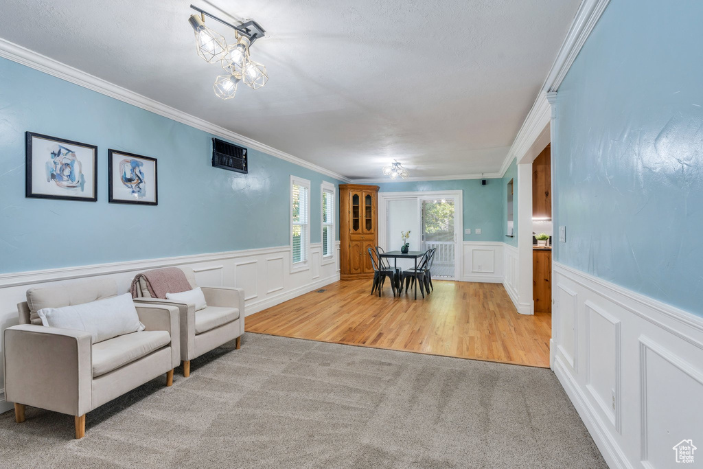 Living area with ornamental molding, a decorative wall, wainscoting, wood finished floors, and carpet floors
