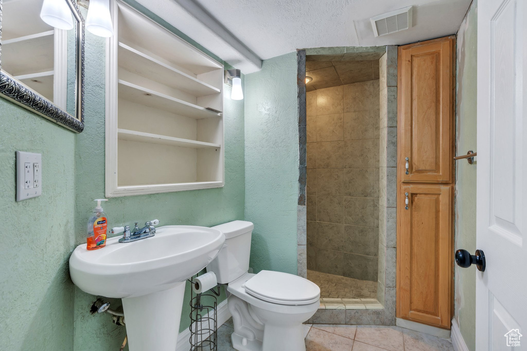 Bathroom with a shower stall, a textured wall, and tile patterned floors