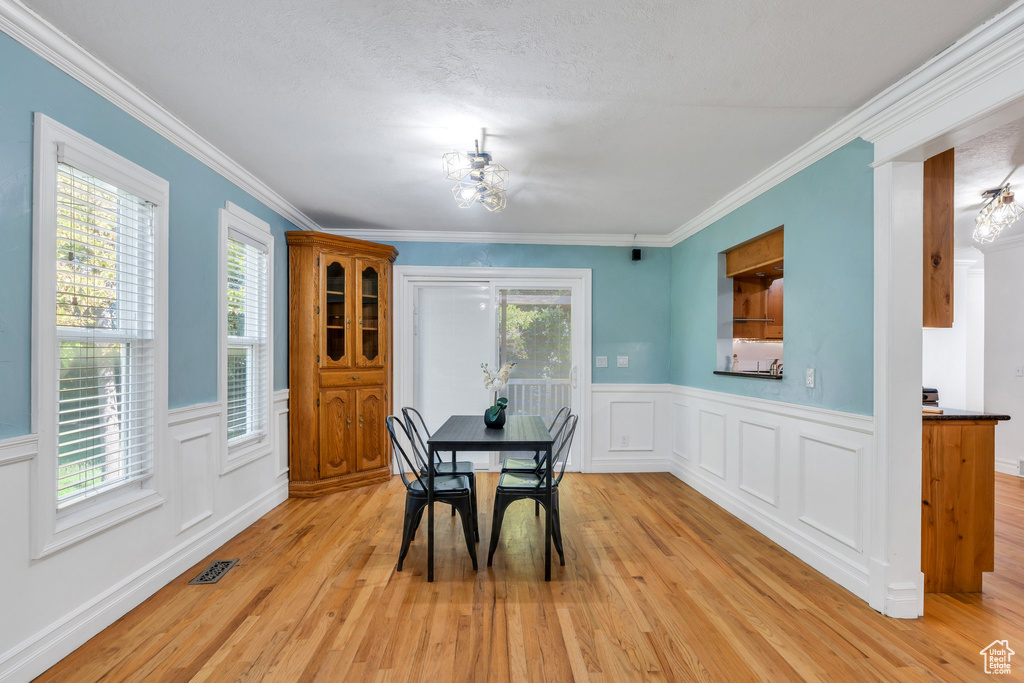 Dining area featuring light wood finished floors, a chandelier, a wainscoted wall, ornamental molding, and a decorative wall