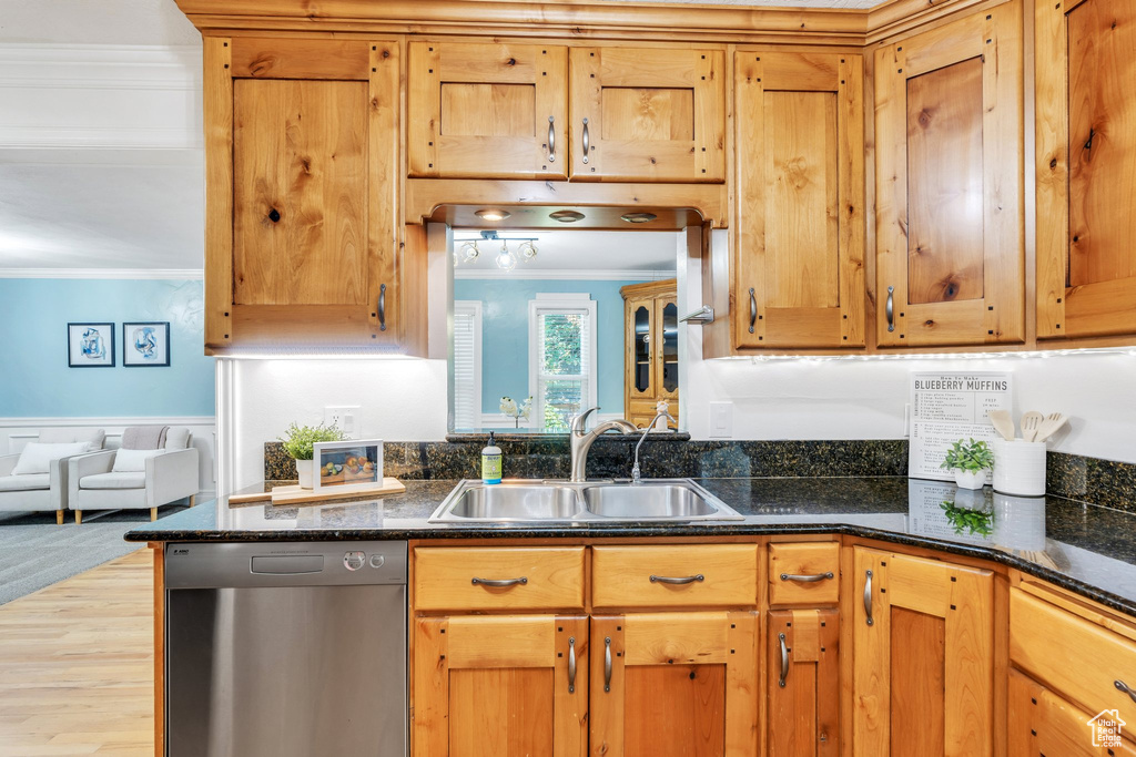 Kitchen with dishwasher, crown molding, wainscoting, dark stone counters, and light wood finished floors