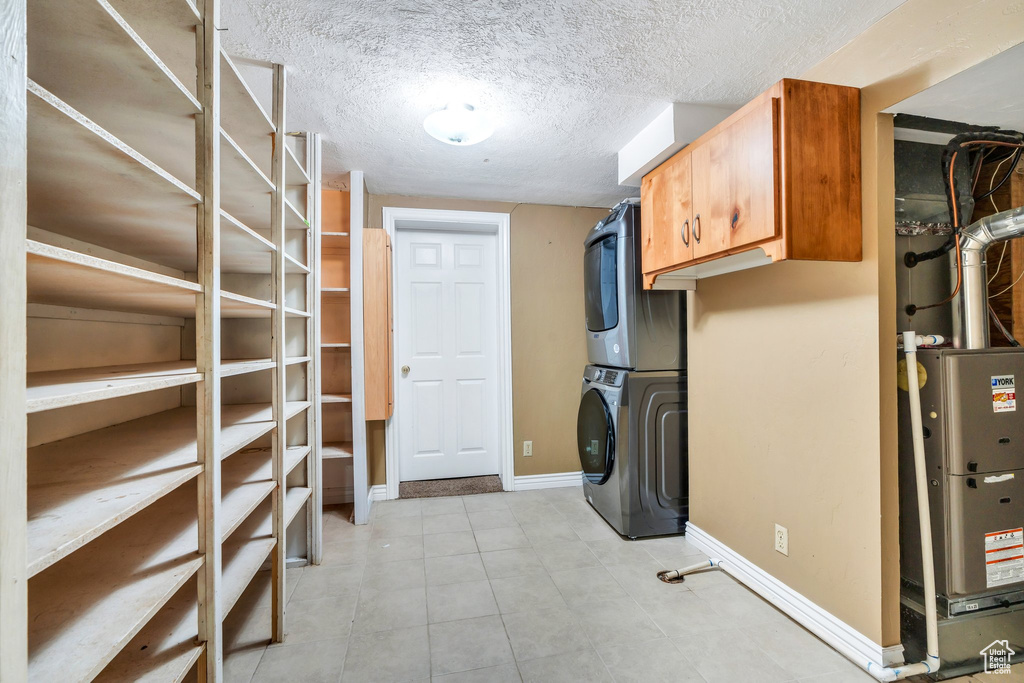 Laundry room featuring stacked washer and clothes dryer, cabinet space, and light tile patterned floors