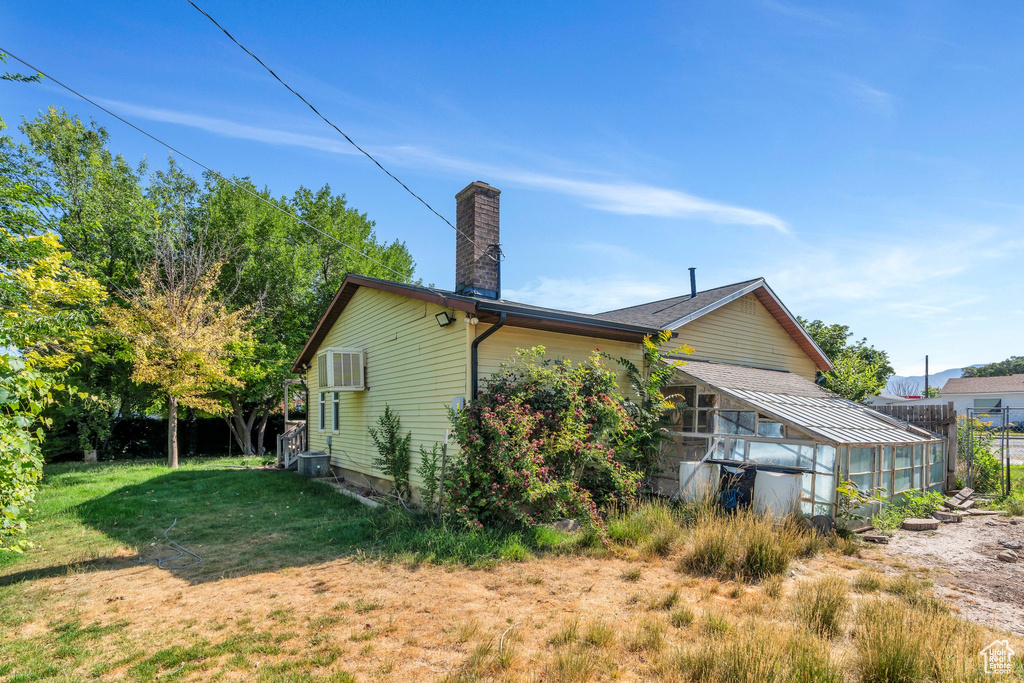 View of side of property featuring a greenhouse, a chimney, an outdoor structure, a wall unit AC, and a yard
