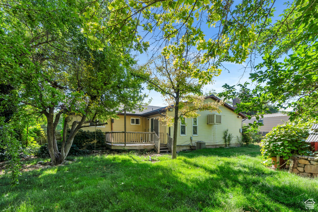 Rear view of house with a deck, a wall mounted air conditioner, and a lawn