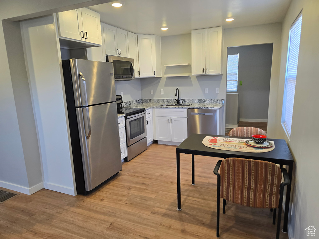 Kitchen with stainless steel appliances, open shelves, light wood-style flooring, white cabinetry, and light stone counters