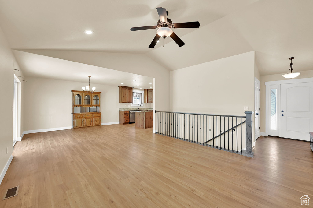 Unfurnished living room with light wood-style flooring, ceiling fan, a chandelier, and vaulted ceiling